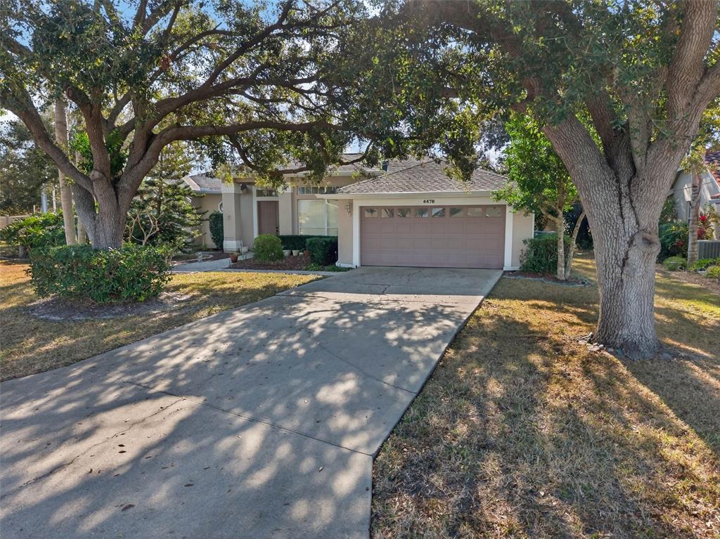 A single-story house with a concrete driveway and large oak trees in the front yard — 4478 PRO AM AVENUE E, BRADENTON, FL