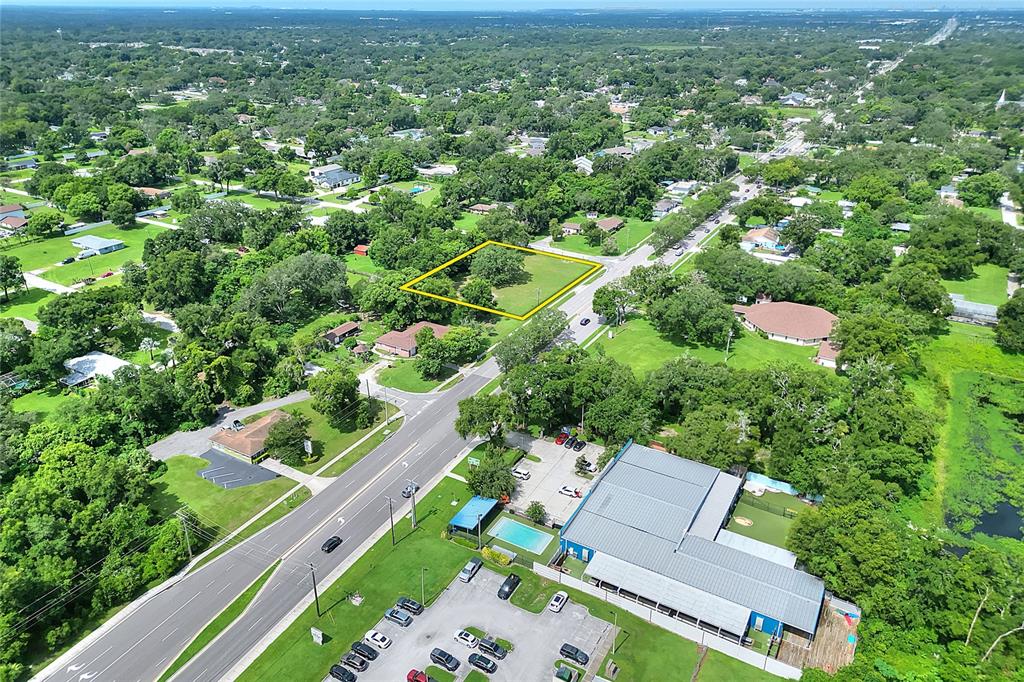 An aerial view shows a vacant, tree-filled lot outlined in yellow near a commercial building — 703 E LUMSDEN ROAD, BRANDON, FL