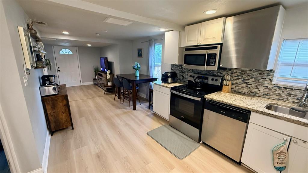 A kitchen features stainless steel appliances, white cabinetry, a mosaic backsplash, and light wood flooring — 313 TAKOMA STREET, ORLANDO, FL