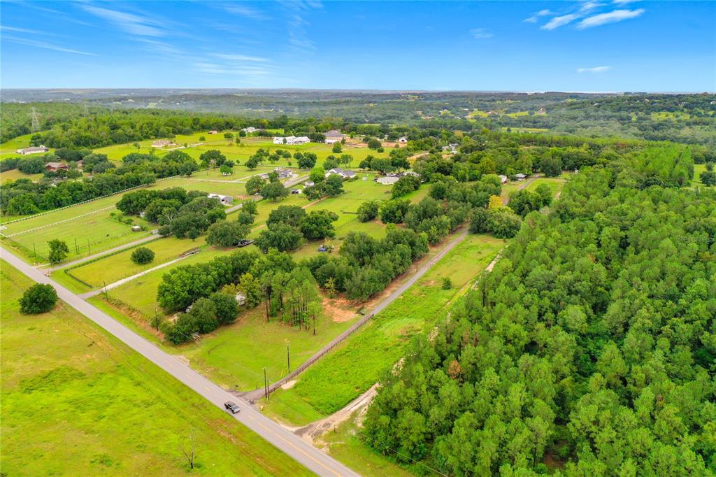 An aerial view shows a rural landscape with a road, open fields, and wooded areas — 13131 COUNTY ROAD 561A, CLERMONT, FL
