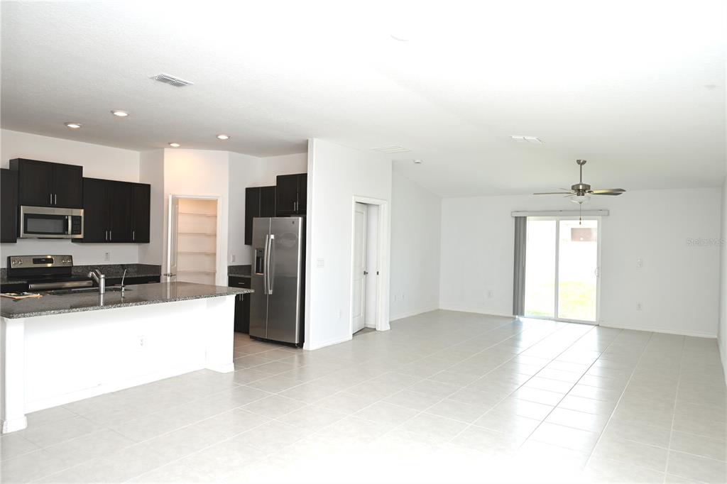 An open-concept kitchen with dark cabinets and granite countertops flows into a spacious tiled living area — 2674 RED EGRET DRIVE, BARTOW, FL