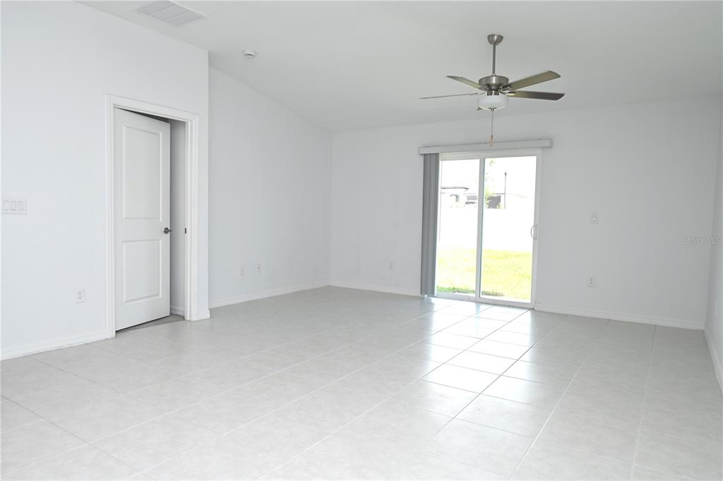 A bright, empty room with white walls, tiled floors, a ceiling fan, and sliding glass doors — 2674 RED EGRET DRIVE, BARTOW, FL