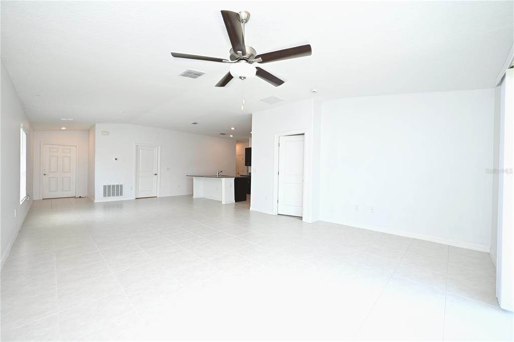 A bright, open-concept living area features white tile floors, a ceiling fan, and a kitchen — 2674 RED EGRET DRIVE, BARTOW, FL