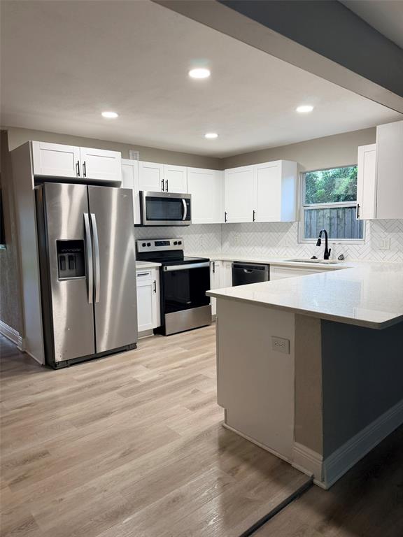 A kitchen features white cabinets, stainless steel appliances, a peninsula, and light wood-look flooring — 1217 E NORFOLK STREET, TAMPA, FL