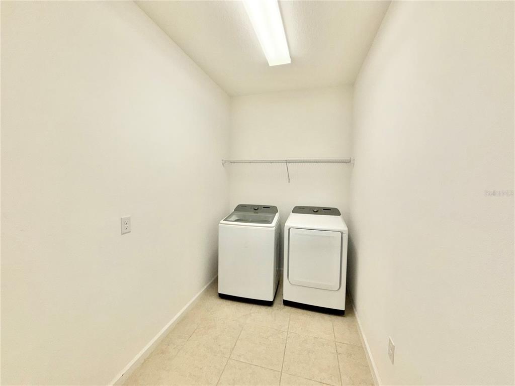 A laundry room features white walls, tile flooring, a wire shelf, and a washer and dryer — 2240 RUSH BAY WAY, ORLANDO, FL