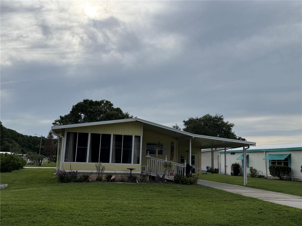 A yellow manufactured home features a screened-in porch, a concrete driveway, and a carport — 101 CYPRESS ROAD, WILDWOOD, FL