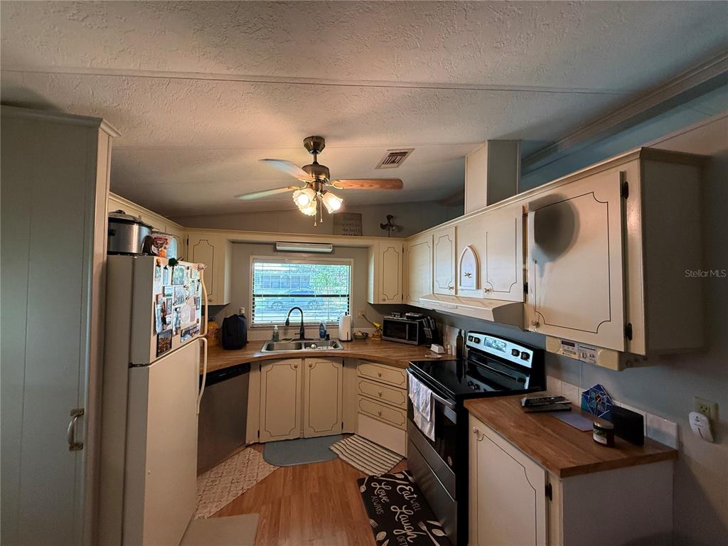 A kitchen with light-colored cabinets and wood countertops opens into a dining area — 101 CYPRESS ROAD, WILDWOOD, FL