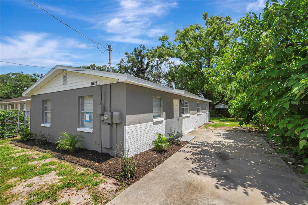 A single-story house with gray stucco and white brick exterior features a concrete driveway — 1615 E SITKA STREET, TAMPA, FL
