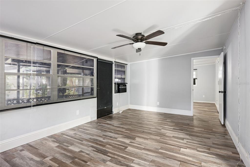 A room with wood-look flooring, a ceiling fan, a large window with blinds, and a doorway — 3000 CLARCONA ROAD UNIT 767, APOPKA, FL