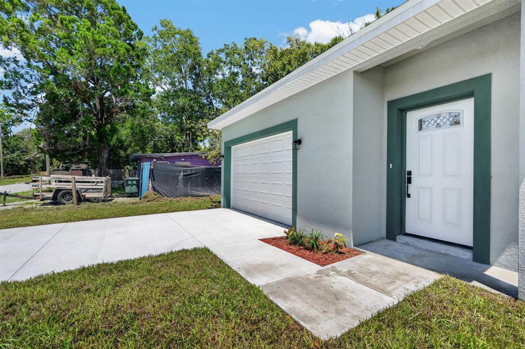 A light gray house exterior features a white garage door, a front door, and landscaping — 757 INDIANA STREET, DAYTONA BEACH, FL