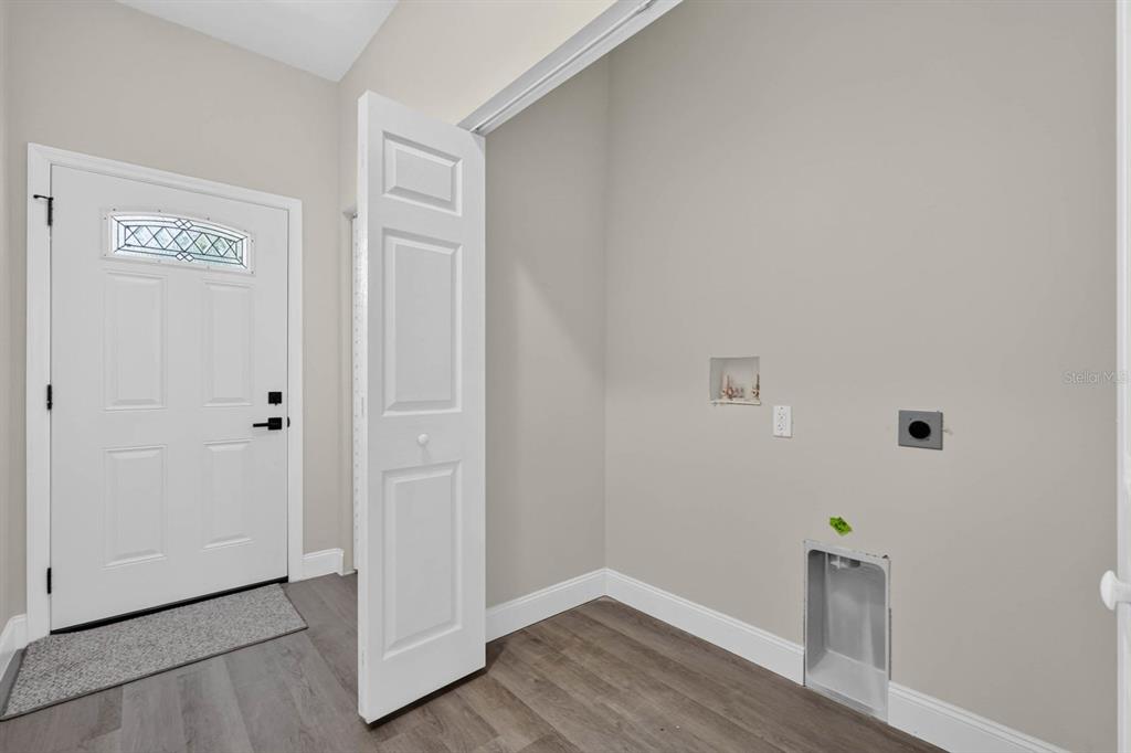 A laundry area with utility hookups, gray wood-look flooring, and an adjacent white entry door — 757 INDIANA STREET, DAYTONA BEACH, FL
