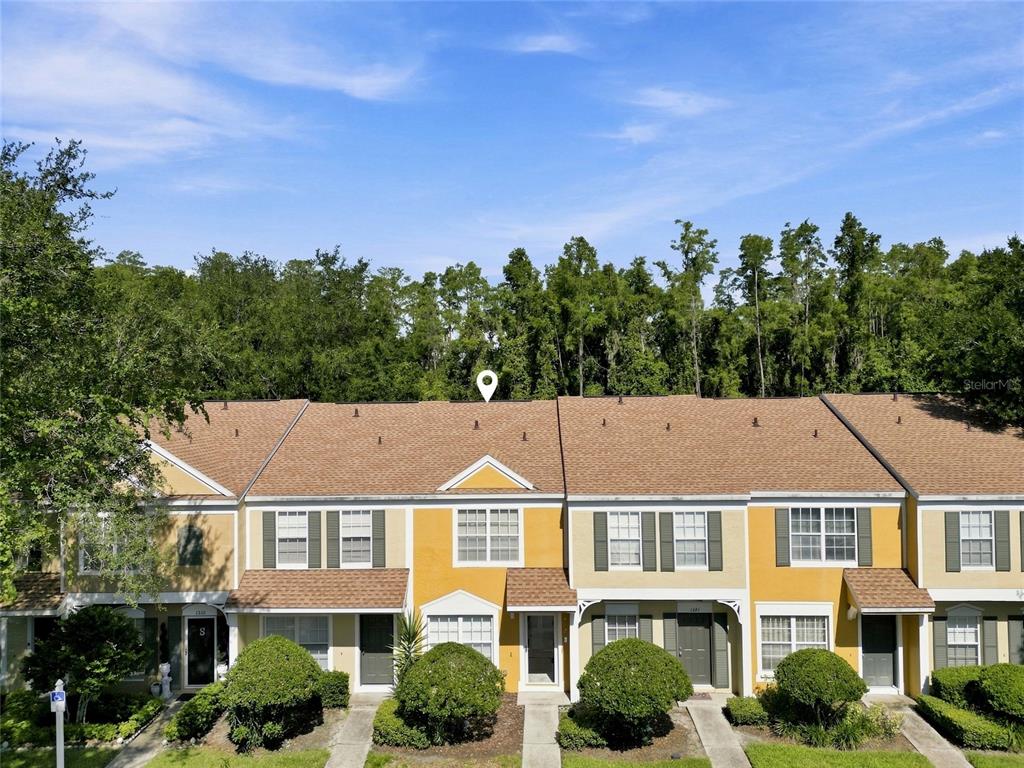 A row of yellow two-story townhomes with brown shingled roofs and green landscaping — 1339 COSTA MESA DRIVE, WESLEY CHAPEL, FL