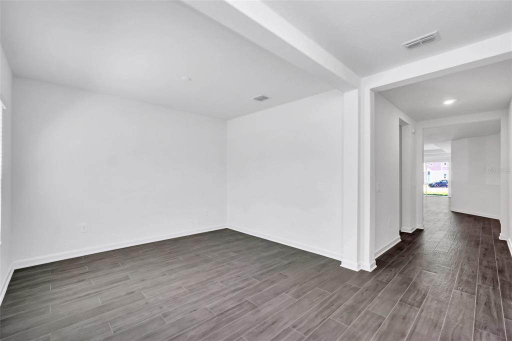 An empty room with white walls and dark wood-look tile flooring leads to a hallway — 5768 STEPHENS ROAD, ST CLOUD, FL