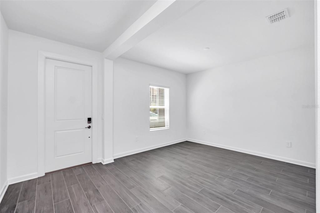 An empty room features white walls, gray wood-look tile flooring, and a single white door — 5768 STEPHENS ROAD, ST CLOUD, FL