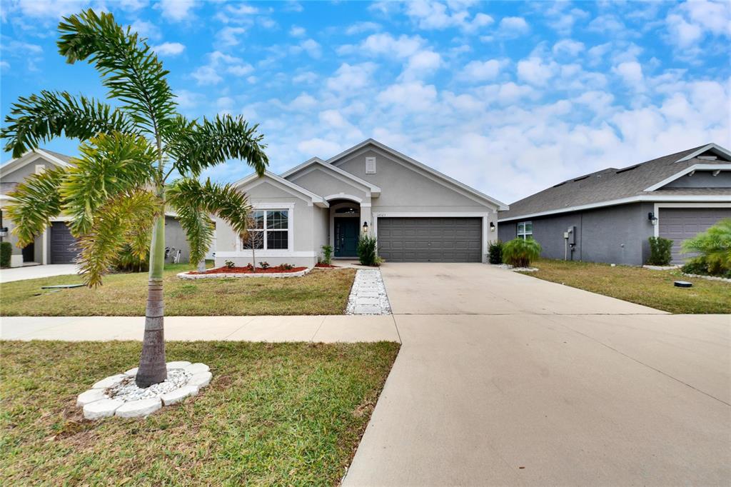 A single-story suburban house with a gray exterior, a two-car garage, and a palm tree — 14525 SCOTTBURGH GLEN DRIVE, WIMAUMA, FL