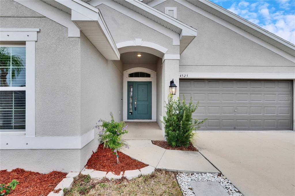 The exterior of a house features a teal front door, a garage, and landscaped beds — 14525 SCOTTBURGH GLEN DRIVE, WIMAUMA, FL