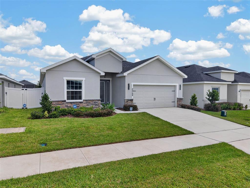 A single-story suburban house with a gray stucco exterior, stone accents, and a two-car garage — 2248 ORCHID DRIVE, DAVENPORT, FL