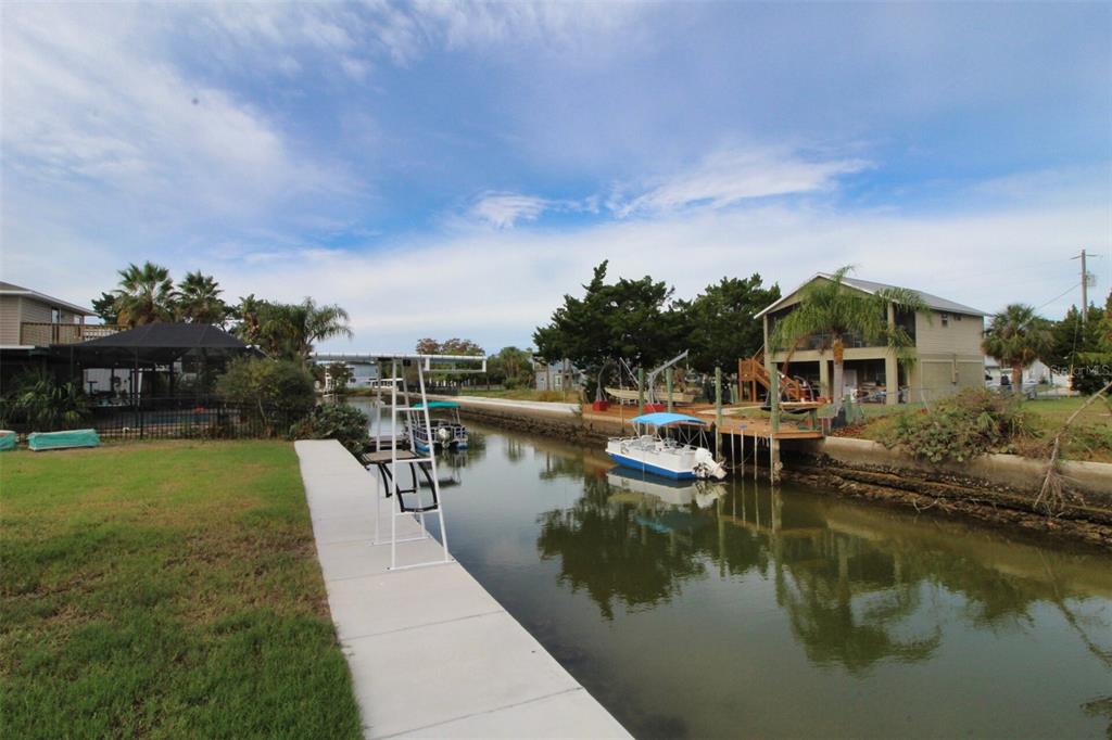 A canal view showing a concrete dock, a boat lift, and a house with palm trees — 4977 CEDARBROOK LANE, HERNANDO BEACH, FL