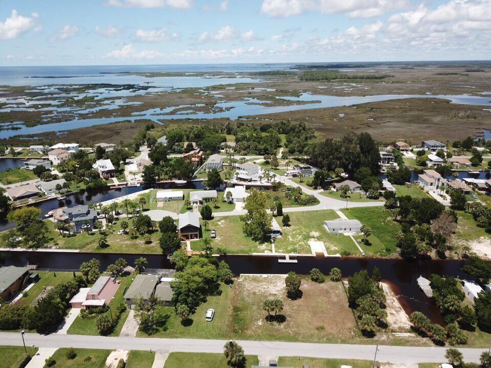 An aerial view shows a waterfront neighborhood with houses, canals, and marshland under a cloudy sky — 4977 CEDARBROOK LANE, HERNANDO BEACH, FL