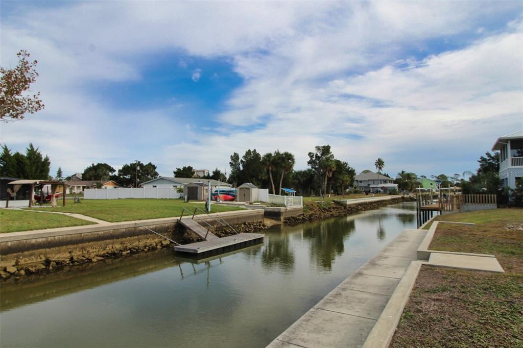A canal view shows a wooden dock, a grassy yard, and residential houses under a sky — 4977 CEDARBROOK LANE, HERNANDO BEACH, FL