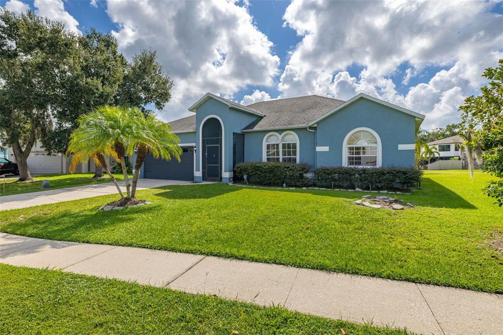 A blue single-story house with a front-facing garage, arched entryway, and a palm tree — 2605 FERN COVE WAY, KISSIMMEE, FL