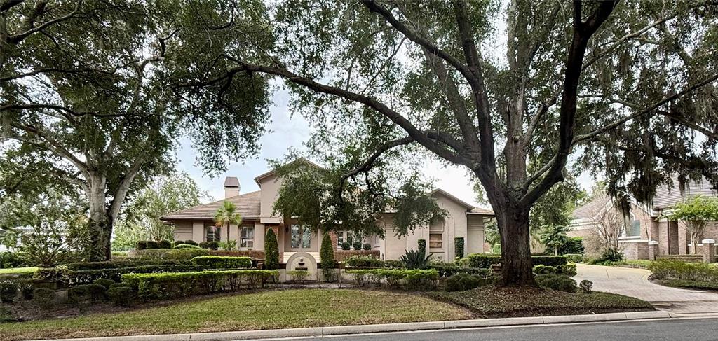 A large, light-colored house sits behind a manicured lawn and mature oak trees — 5379 ISLEWORTH COUNTRY CLUB DRIVE, WINDERMERE, FL