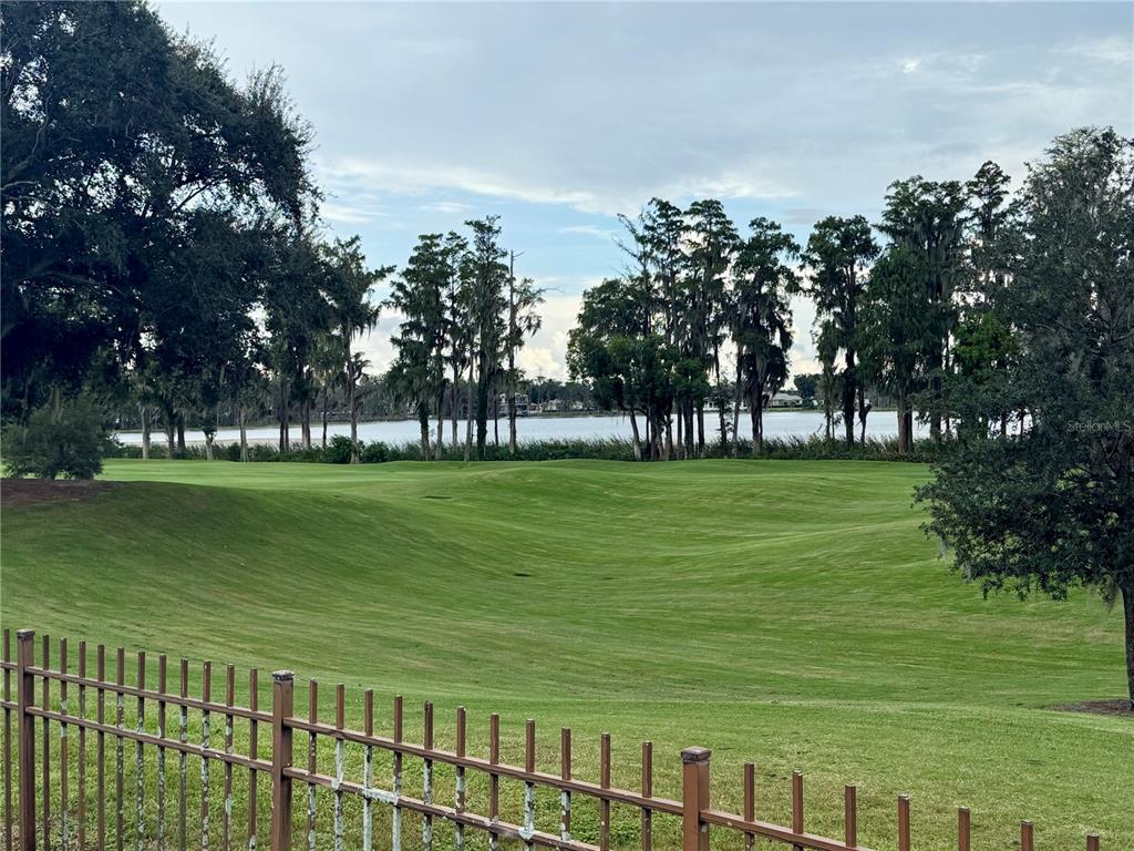 A grassy lawn slopes down toward a lake bordered by tall trees under a cloudy sky — 5379 ISLEWORTH COUNTRY CLUB DRIVE, WINDERMERE, FL