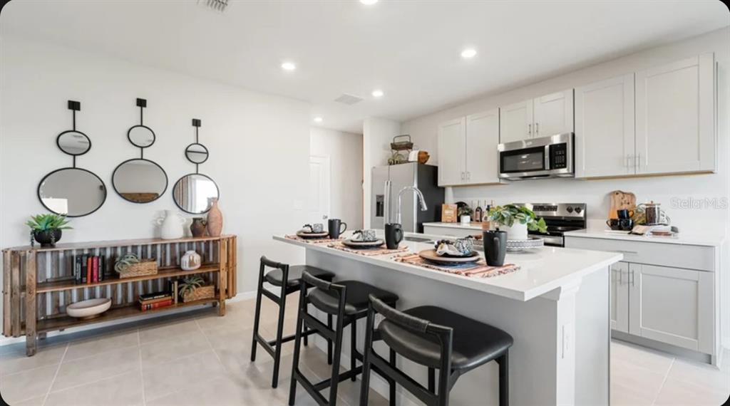 A modern kitchen features white cabinets, stainless steel appliances, a center island, and dining area — 9308 CHISWELL TRAIL, PALMETTO, FL