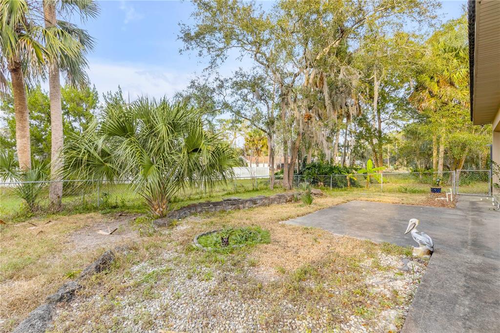 A backyard features a concrete patio, a small stone retaining wall, and a pelican statue — 12 PEARL DRIVE, ORMOND BEACH, FL
