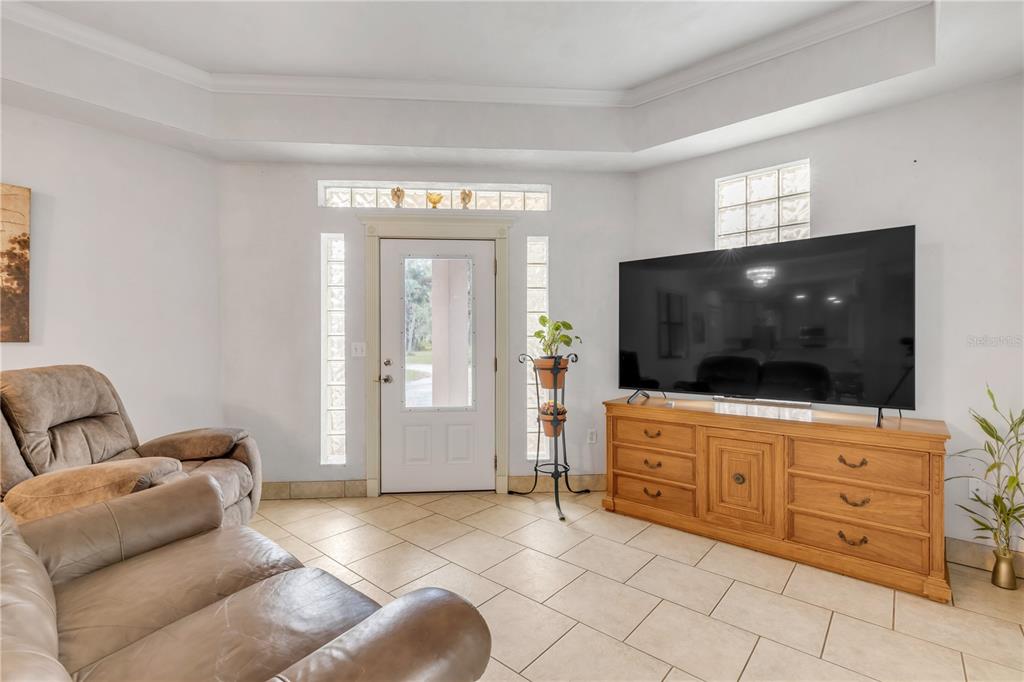 A living room features a television on a wooden console, tile flooring, and glass blocks — 12 PEARL DRIVE, ORMOND BEACH, FL