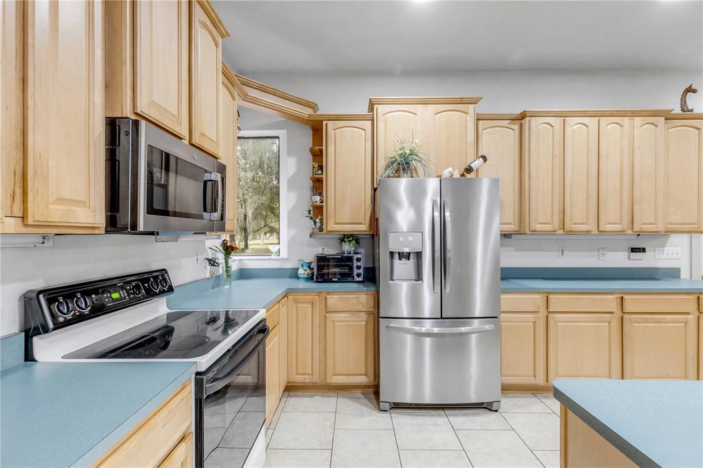 A kitchen features light wood cabinets, stainless steel appliances, and blue laminate countertops — 12 PEARL DRIVE, ORMOND BEACH, FL