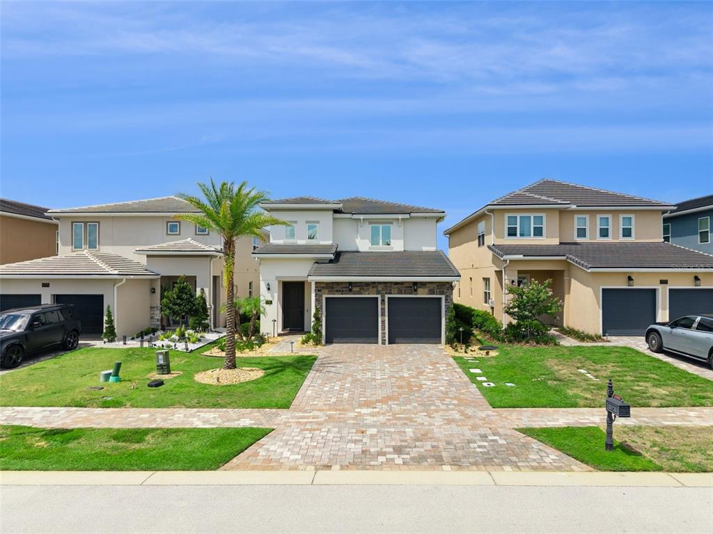 A street-level view of three modern two-story suburban houses with paved driveways and lawns — 15702 VETTA DRIVE, MONTVERDE, FL