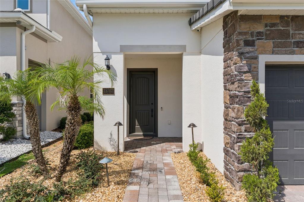 A paved walkway leads to the front entrance of a house with stone accents — 15702 VETTA DRIVE, MONTVERDE, FL