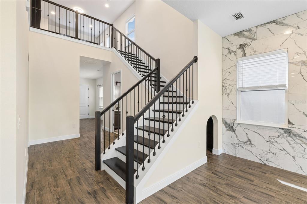 A staircase with dark wood treads and black railings stands in a room with marble-tiled walls — 15702 VETTA DRIVE, MONTVERDE, FL