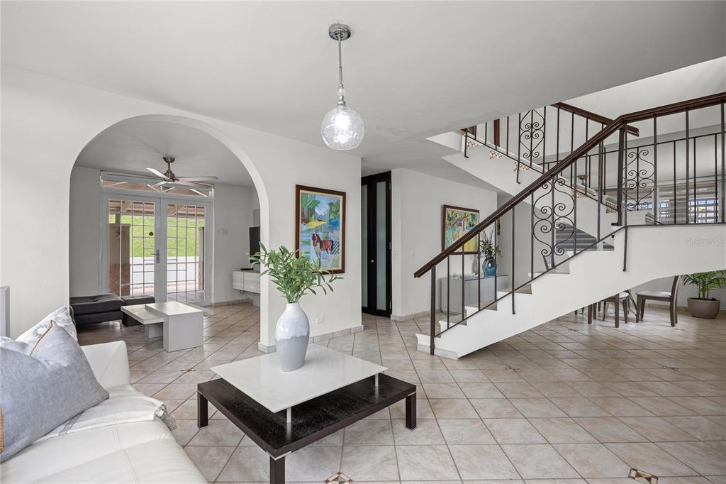 A living room with tile floors, a white sofa, and a staircase with iron railings — Calle 6 H17 TINTILLO GARDENS, GUAYNABO, PR