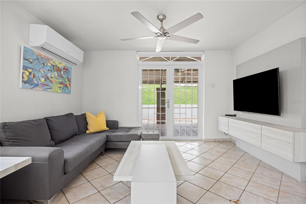 A living room features a gray sectional sofa, a television, and glass doors to a patio — Calle 6 H17 TINTILLO GARDENS, GUAYNABO, PR