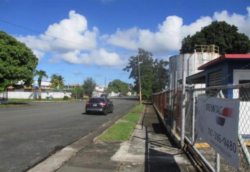 A street view shows a sidewalk, a chain-link fence, and a large industrial water tank — Warehouse JARDINES CAROLINA, ROSENDO VELA ACOSTA ST. UNIT 6A & 6B, CAROLINA, PR