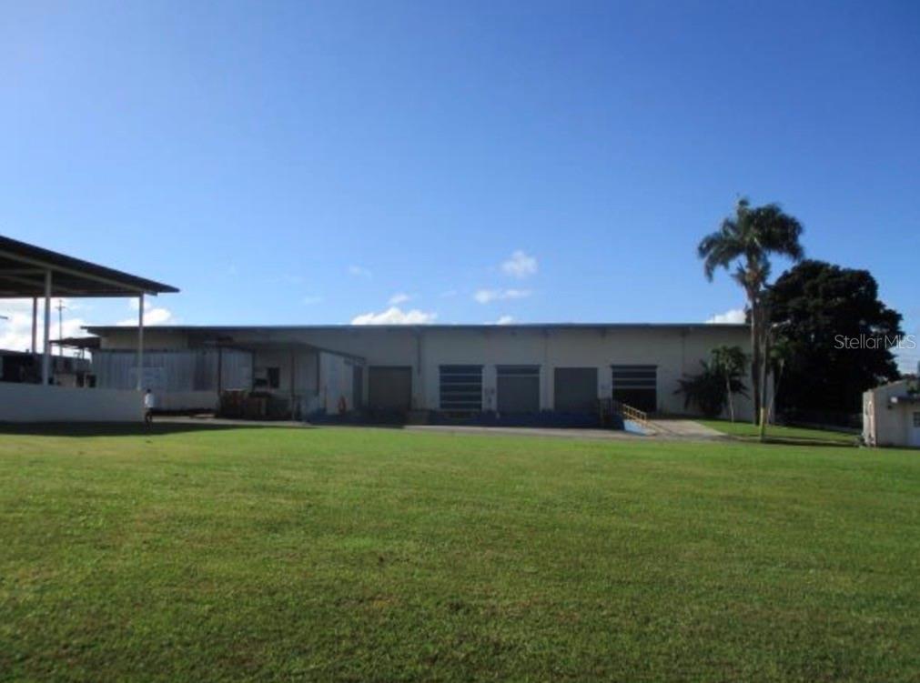 A large, single-story industrial warehouse building sits behind a wide, open grassy lawn — Warehouse JARDINES CAROLINA, ROSENDO VELA ACOSTA ST. UNIT 6A & 6B, CAROLINA, PR