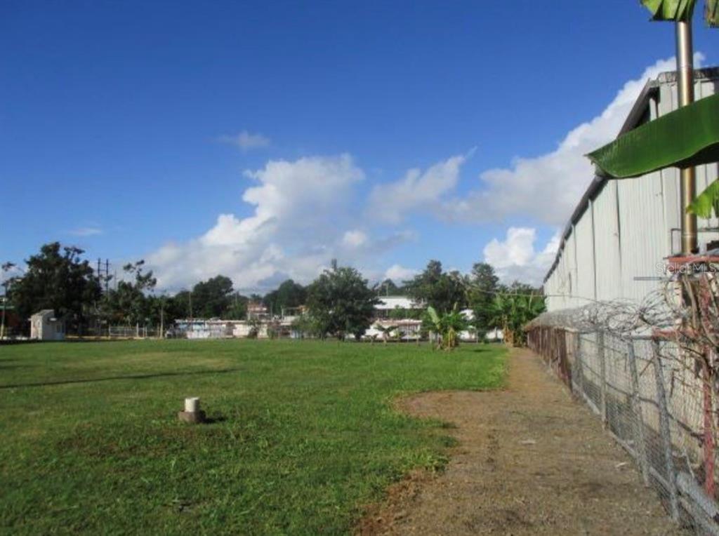 A grassy lot sits next to a metal building enclosed by a chain-link fence — Warehouse JARDINES CAROLINA, ROSENDO VELA ACOSTA ST. UNIT 6A & 6B, CAROLINA, PR
