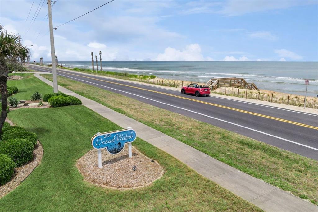 A red convertible drives on a coastal road past an Ocean Watch sign and beach — 2700 OCEAN SHORE BOULEVARD UNIT 405, ORMOND BEACH, FL