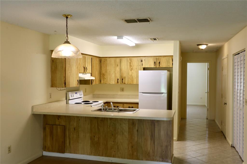 A kitchen with wood cabinets, white appliances, and a breakfast bar overlooking a hallway — 54 FOREST ROAD UNIT 54, FLAGLER BEACH, FL