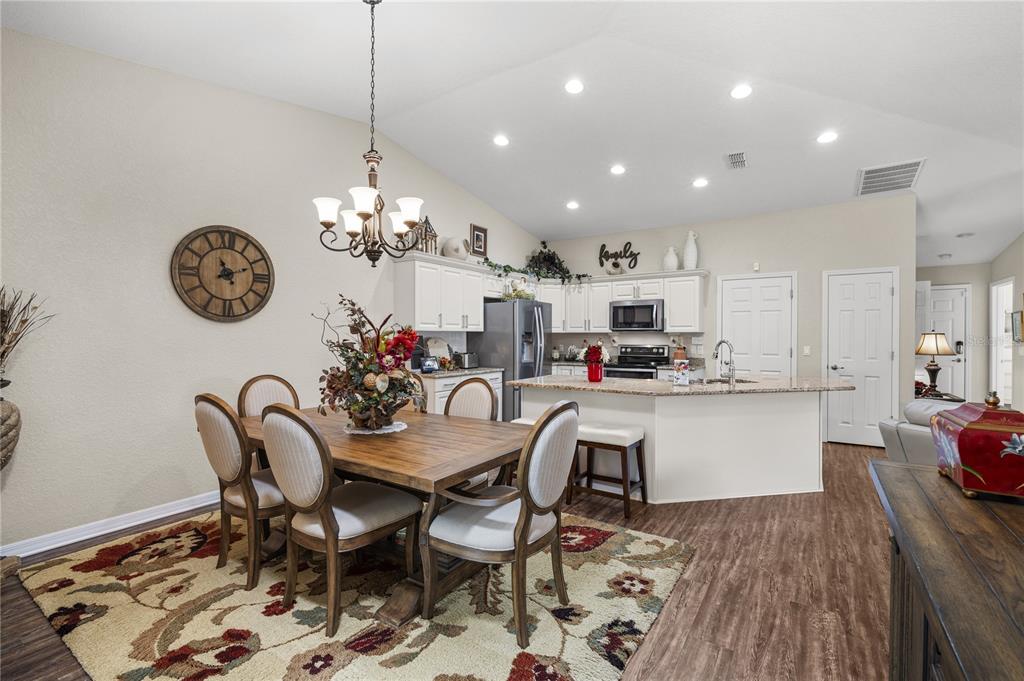 A dining area with a wooden table and chairs sits adjacent to an open kitchen — 6781 BASSWOOD CIRCLE, ZEPHYRHILLS, FL