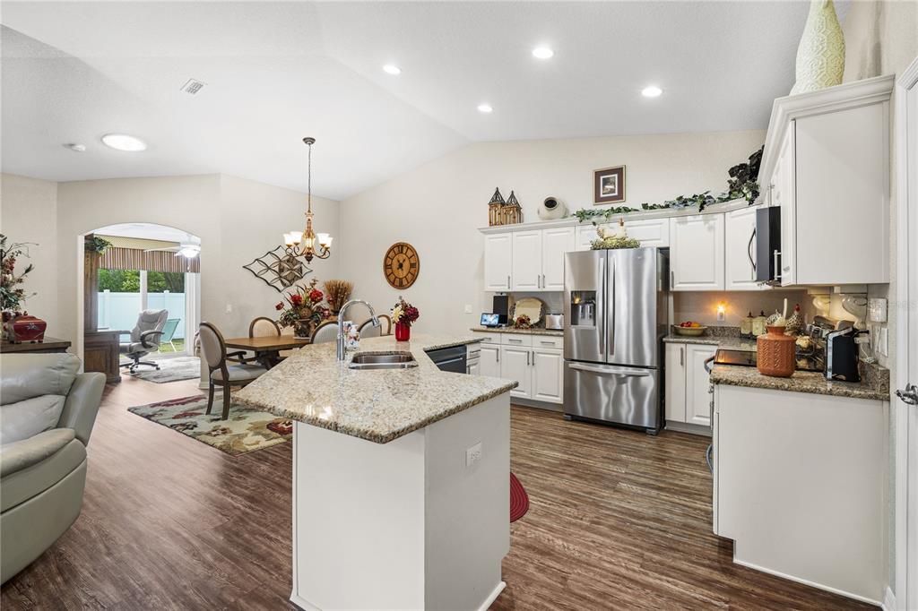 A kitchen with white cabinets, granite countertops, and stainless steel appliances opens to a dining area — 6781 BASSWOOD CIRCLE, ZEPHYRHILLS, FL