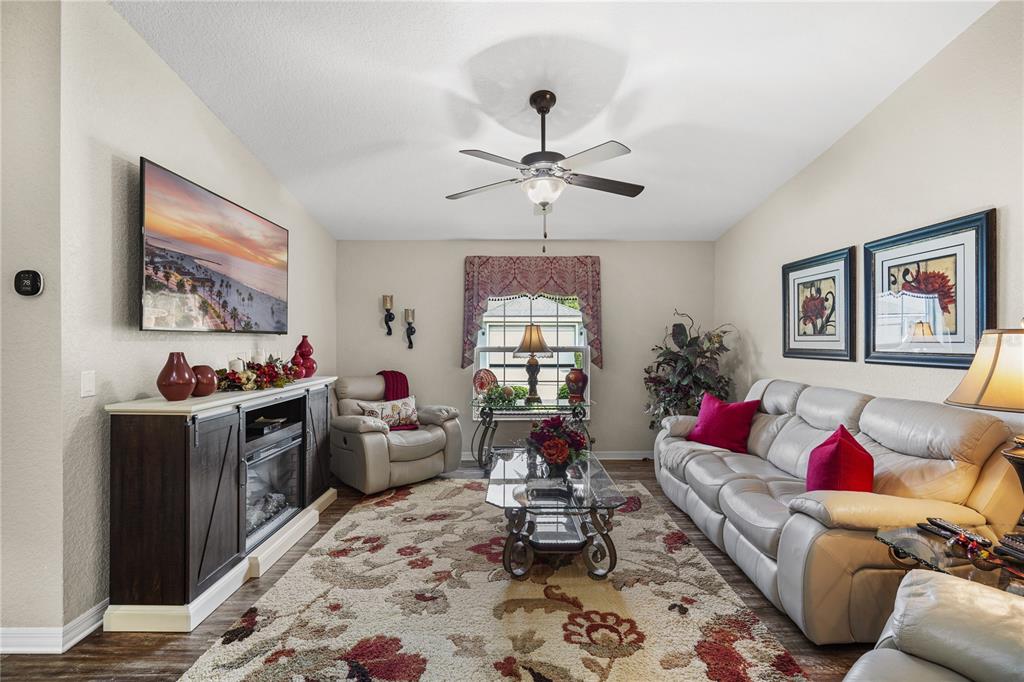 A living room features a fireplace console, a light-colored sofa, and a floral area rug — 6781 BASSWOOD CIRCLE, ZEPHYRHILLS, FL