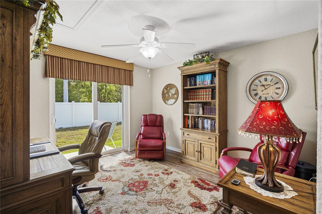 A home office features a desk, two red recliners, a bookshelf, and a sliding glass door — 6781 BASSWOOD CIRCLE, ZEPHYRHILLS, FL