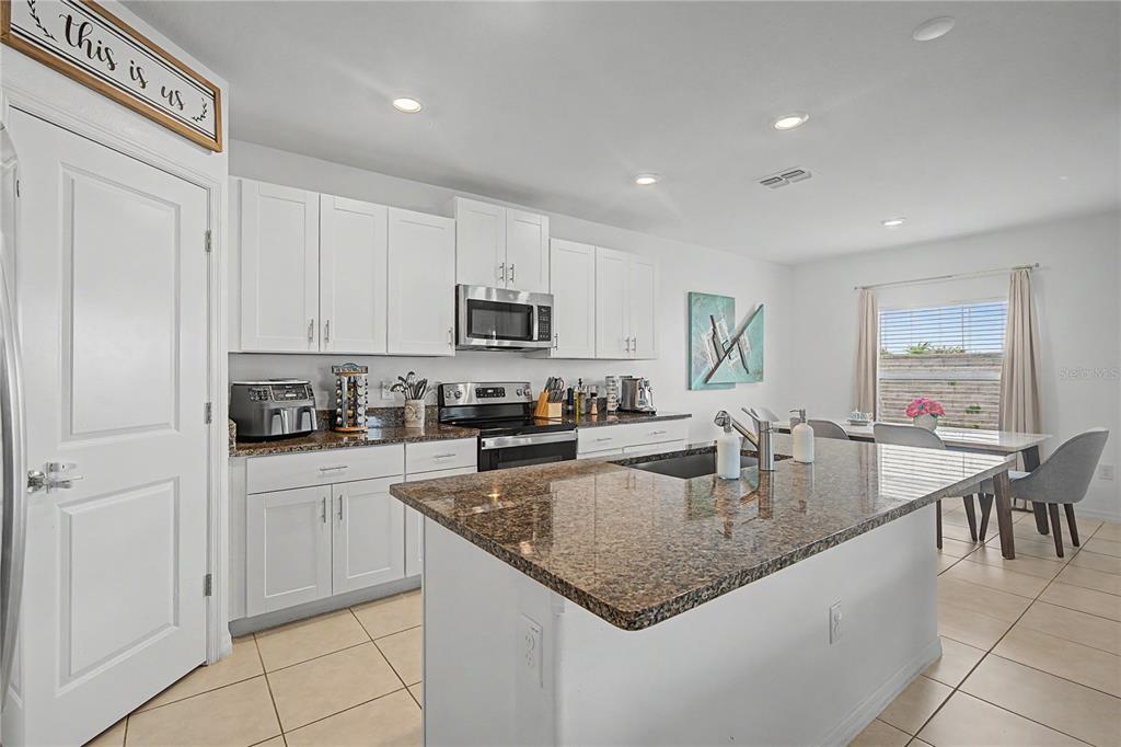 A kitchen with white cabinets, granite countertops, a center island, and tile flooring — 6357 BEVERLY HILLS DRIVE, ZEPHYRHILLS, FL