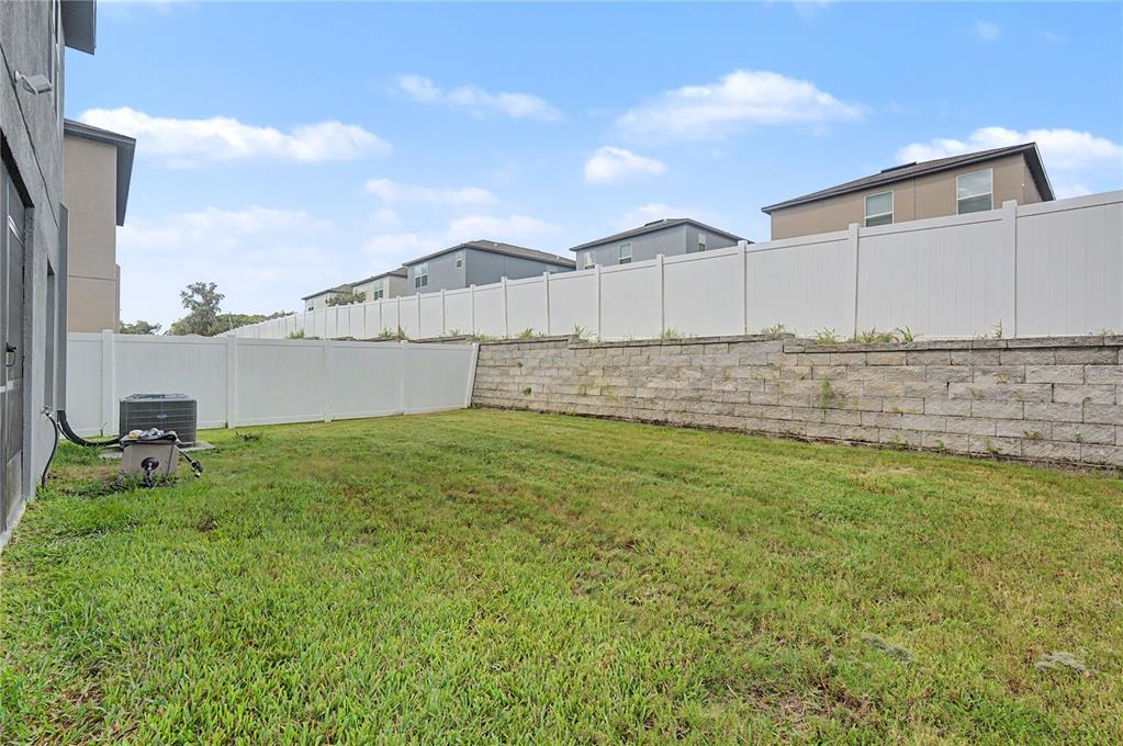 A grassy backyard features a white vinyl fence and a stone retaining wall — 6357 BEVERLY HILLS DRIVE, ZEPHYRHILLS, FL