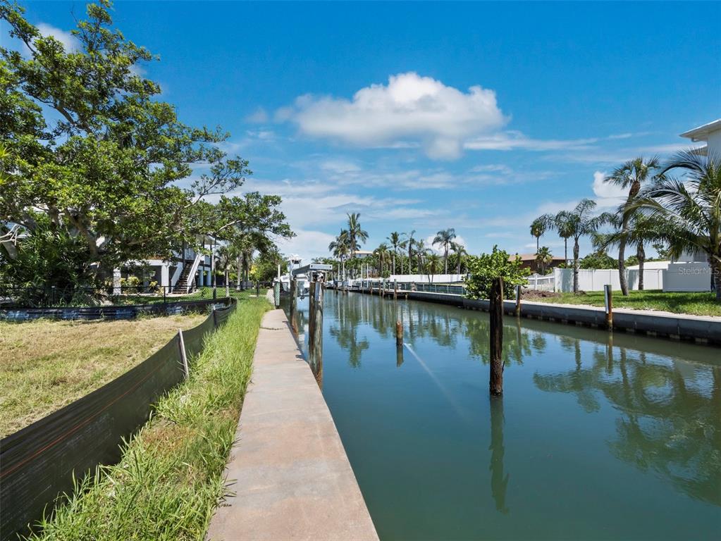 A concrete walkway runs alongside a narrow canal lined with wooden pilings and palm trees — 570 DE NARVAEZ DRIVE, LONGBOAT KEY, FL