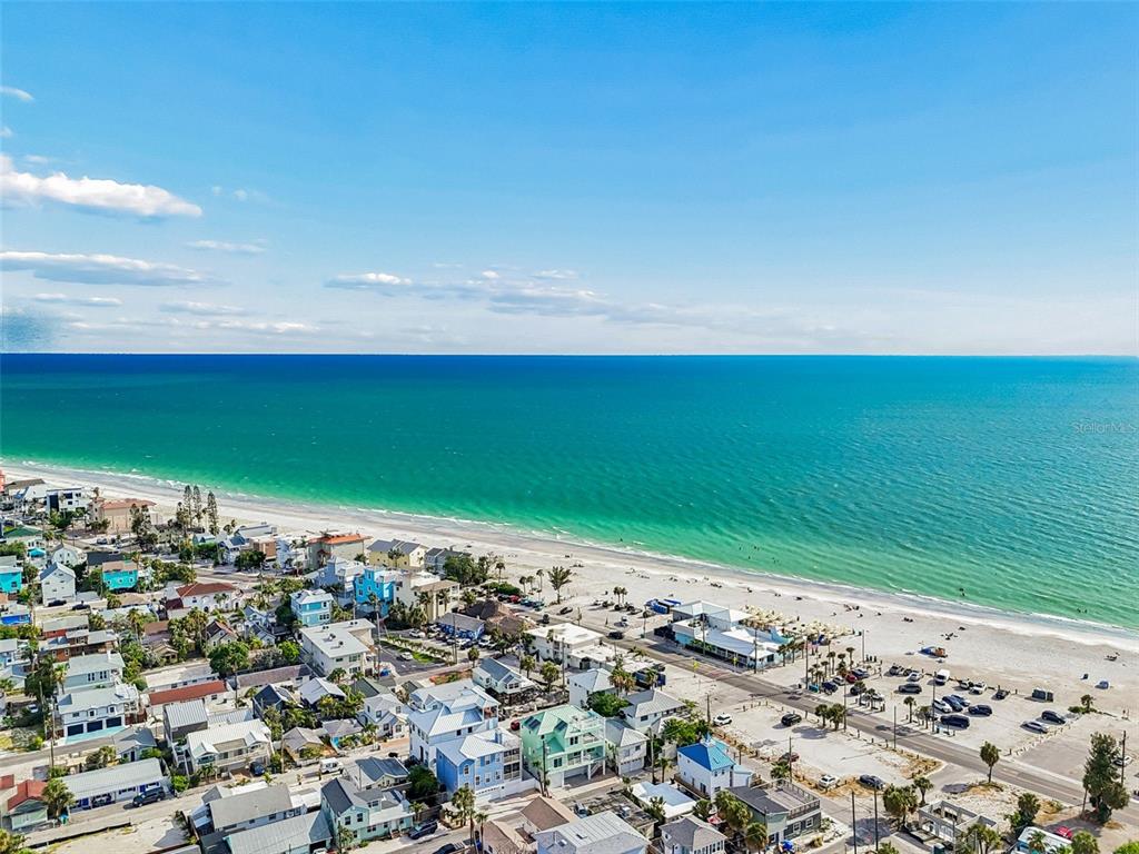 An aerial view shows a light green house with solar panels near a sandy beach — 111 91ST AVENUE, TREASURE ISLAND, FL