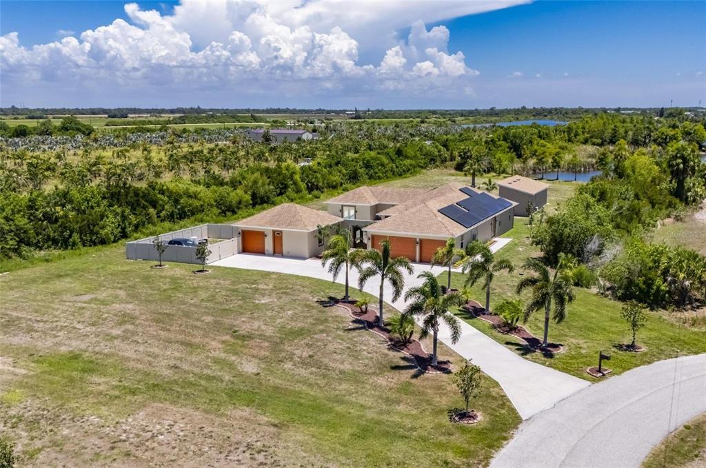 An aerial view of a suburban house with a large yard, solar panels, and palm trees — 3016 SMILODON TRAIL, RUSKIN, FL